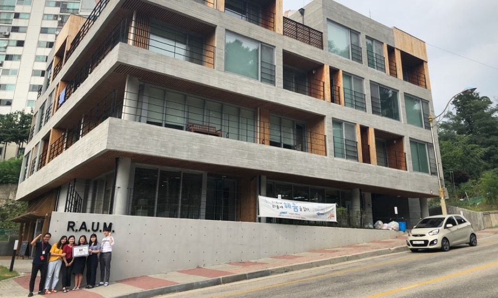 Six people are taking a commemorative photo in front of the entrance with a view of the R.A.U.M. building.