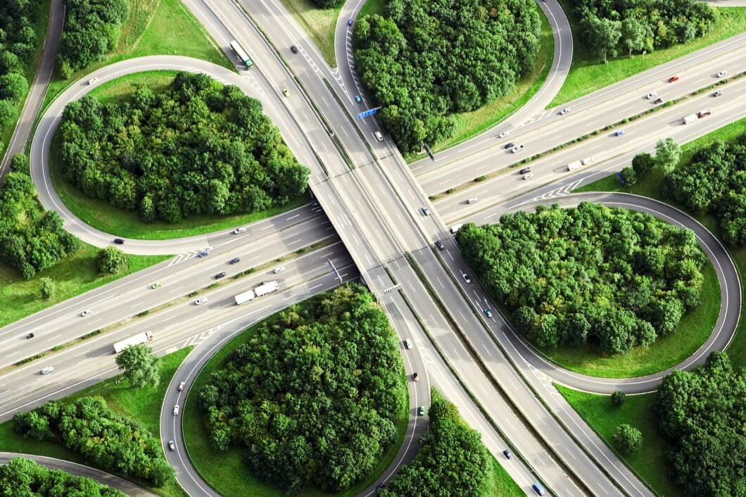 Sky view of cloverleaf interchange with trees between the interchange and the highway.
